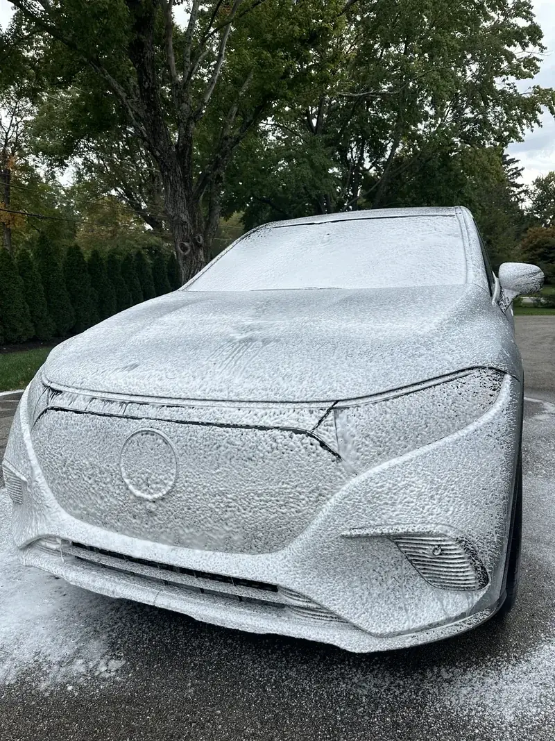 A silver SUV covered in foam from the foam cannon, parked in a driveway