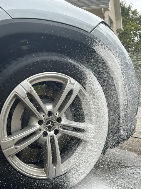 A car wheel and tire covered in white foam during an exterior detail
